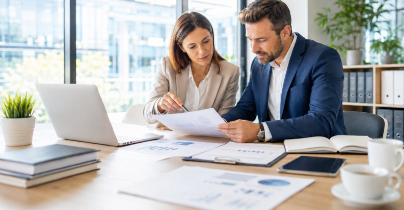 Zwei Fachpersonen prüfen gemeinsam Unternehmensdaten und Analyseunterlagen in einem hellen, modernen Büro.